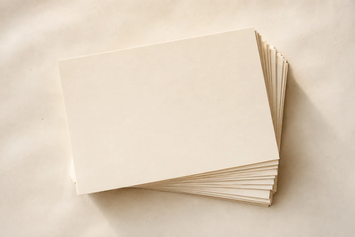 A neat stack of blank cream cards fanned slightly on warm off-white paper.