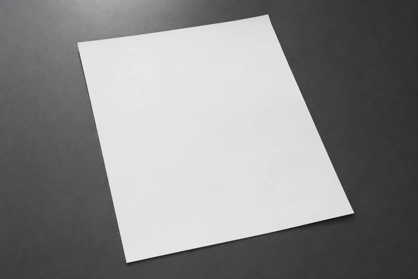 A freshly printed blank sheet of office paper on a matte dark grey desk.