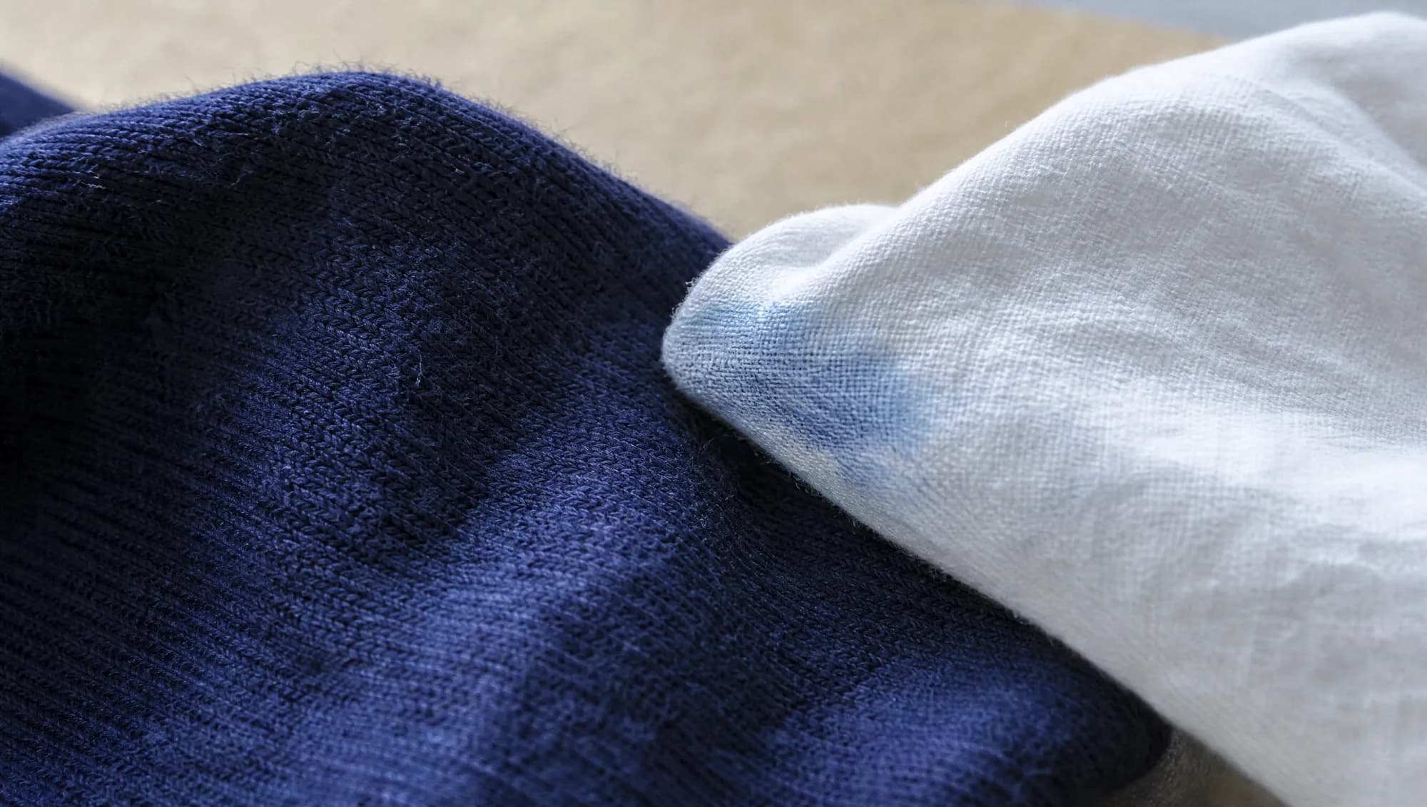A damp white cotton cloth lifted away from a deep indigo merino knit, with a faint pale blue mark left across the cloth.