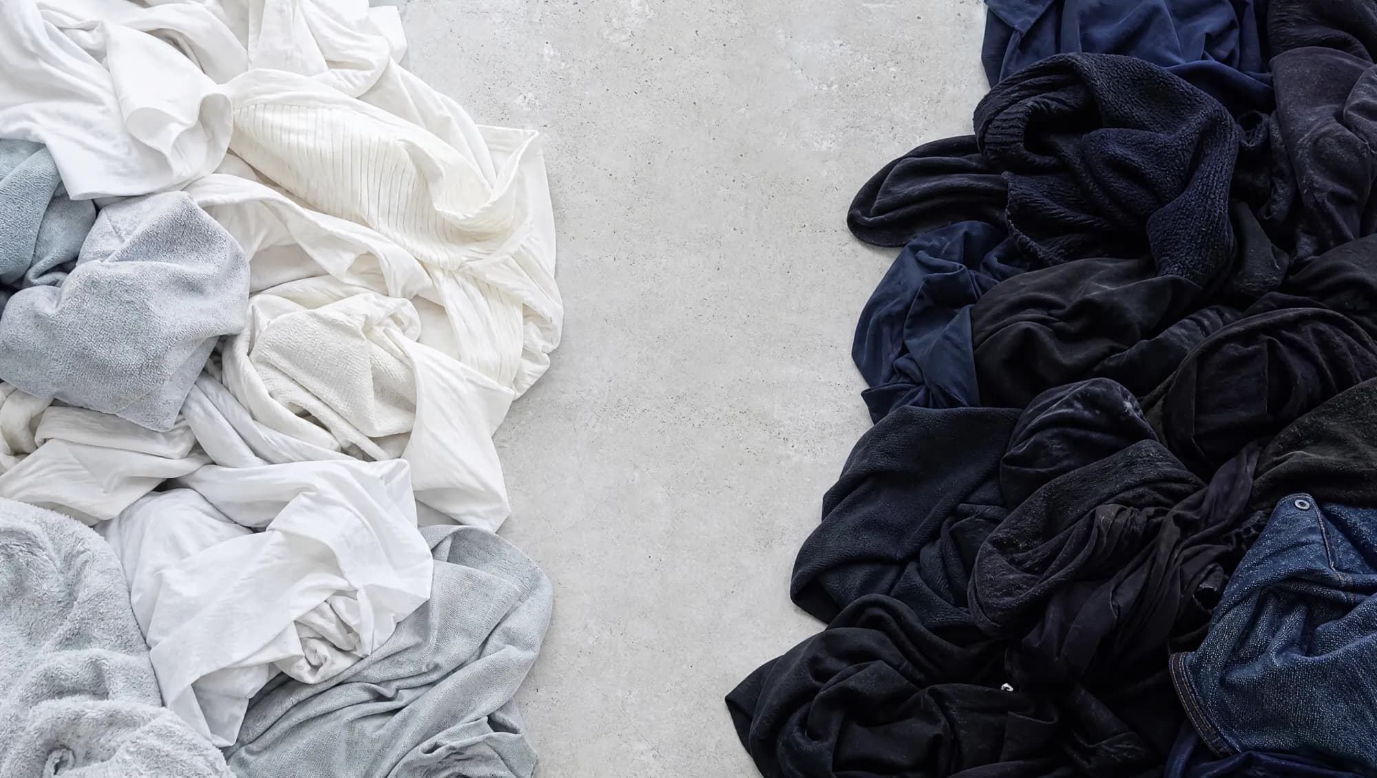 A laundry pile sorted into whites and pale greys on one side and deep indigo and black on the other.