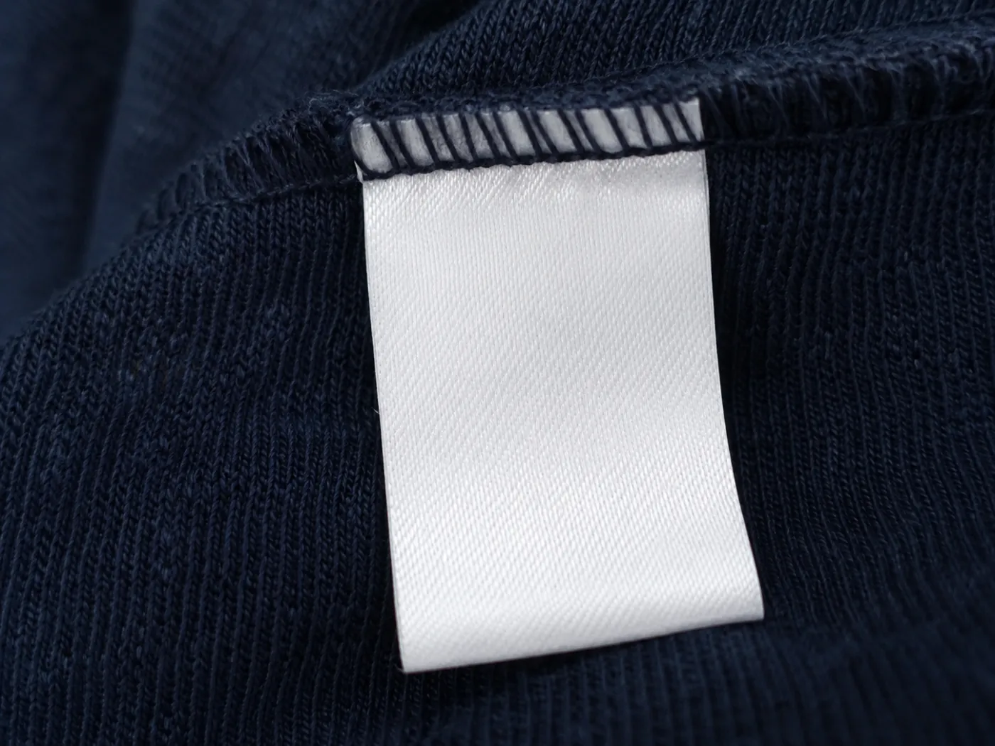 A blank woven care label tape turned out from the inside seam of a dark indigo knitted garment.