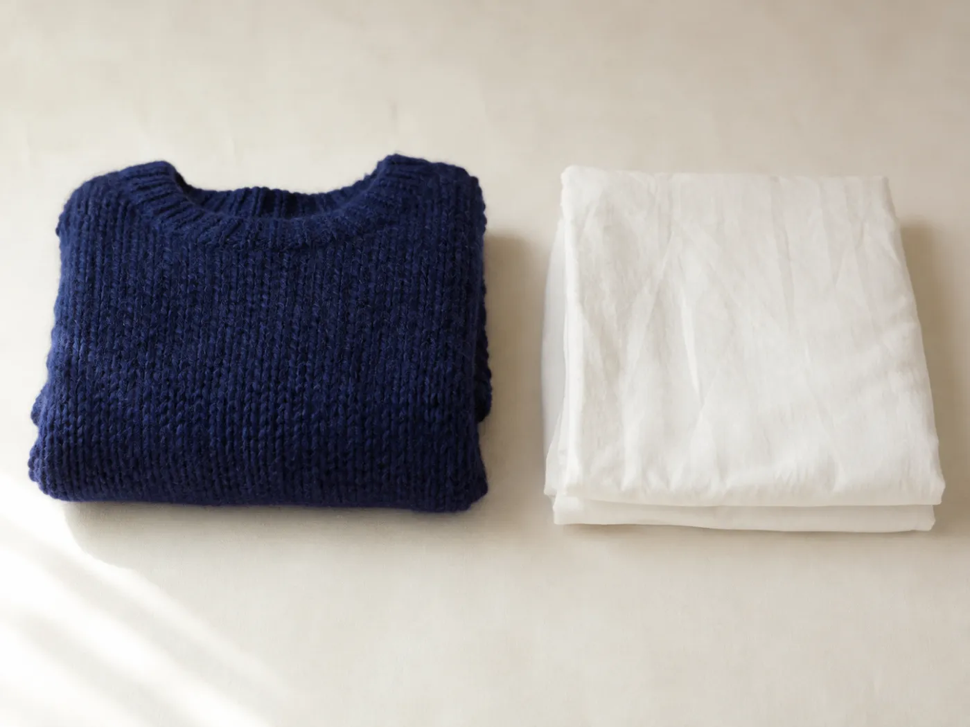 A folded deep indigo merino knit beside a folded plain white cotton cloth on warm off-white paper.