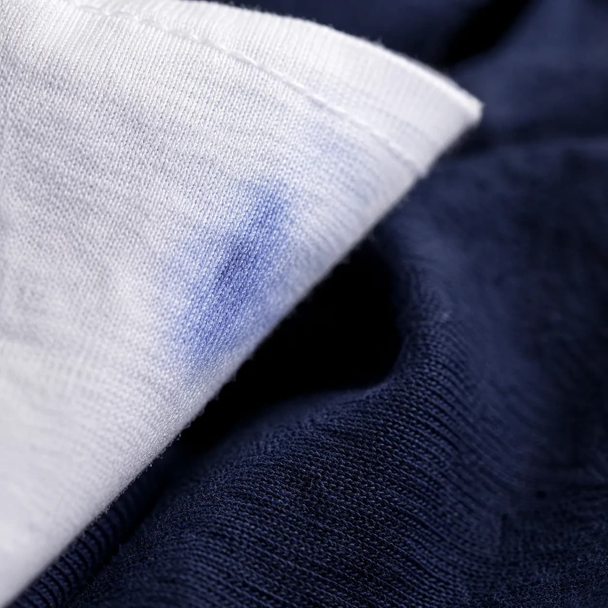 A white cotton cloth being lifted away from a deep indigo knit, showing a faint blue mark.